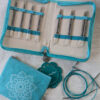 Étui ouvert du kit d’aiguilles circulaires interchangeables KnitPro Mindful Believe, montrant les pointes métalliques de 3 à 6 mm rangées par taille, accompagnées de câbles et accessoires turquoise.