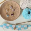 photo d'un ouvrage en crochet avec un marqueur de mailles en bois décoré de fleurs en micro crochet, à l'arrière plan une assiette en bois dans lequel se trouve d'autres marqueurs de mailles en bois et des pelotes de laine