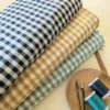 tissu vichy enroulé de couleur bleu marine, jaune et vert menthe en premier plan il y a deux bobines de fils de couture et ciseaix coupe-fil