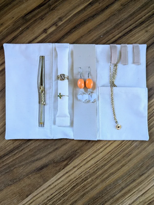 Intérieur de la trousse à bijoux nomade avec poche zippée, support pour bagues, boucles d’oreilles et colliers.
