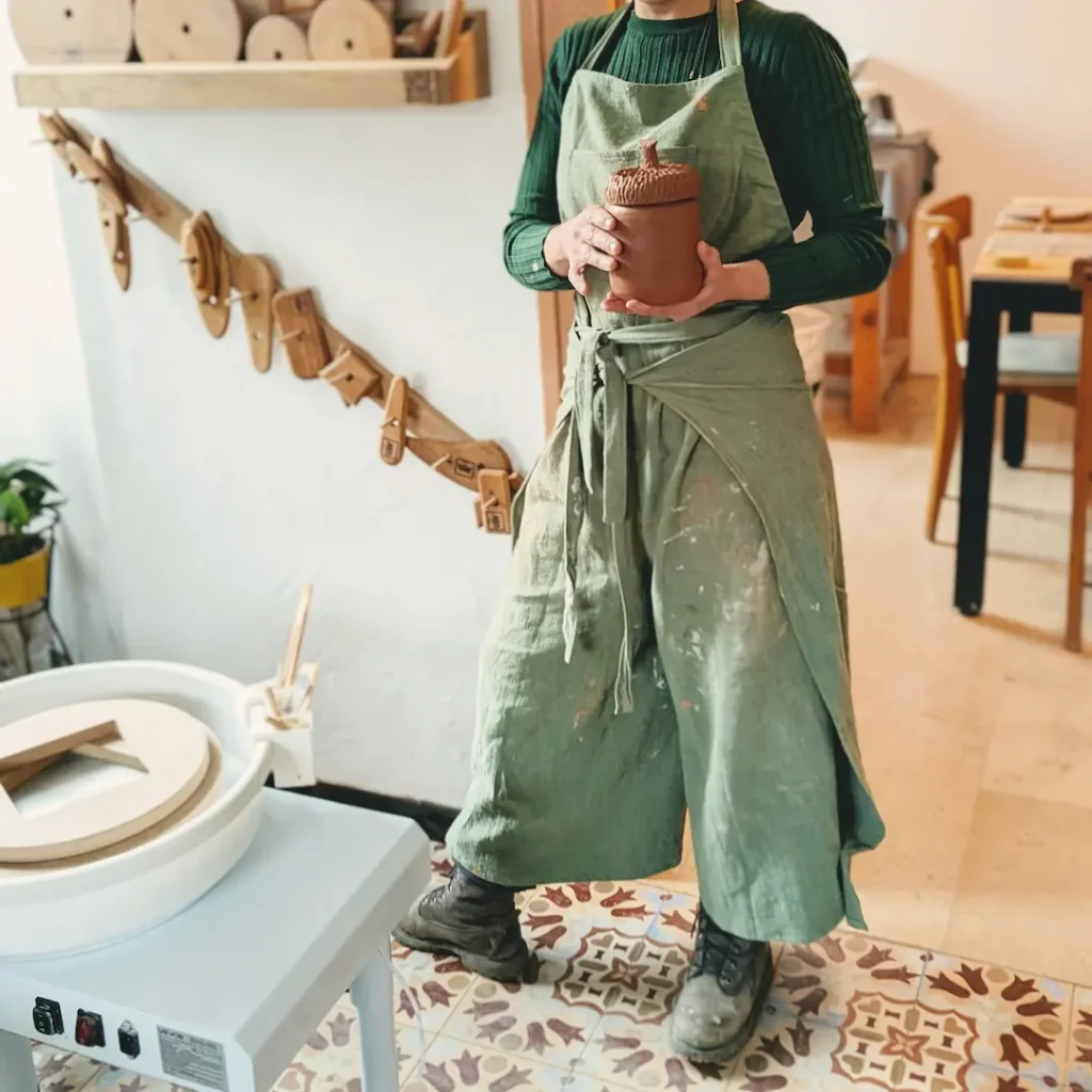 Artisane portant un tablier de poterie vert en tissu dans son atelier de céramique.
