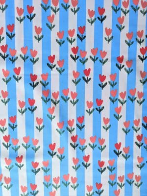 Tissu coton Tulip à tulipes rouges et roses sur rayures bleu ciel et écru. Un imprimé fleuri et coloré pour vêtements et accessoires. Laize 150 cm.