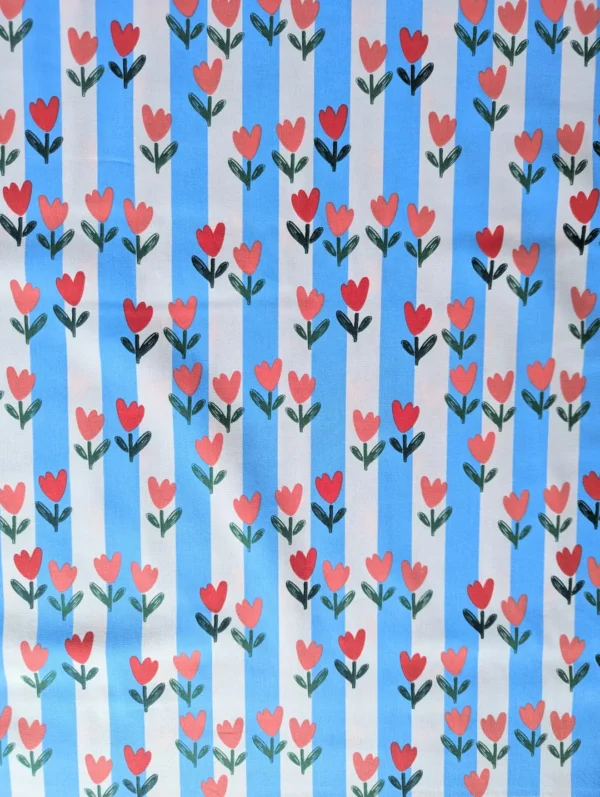 Tissu coton Tulip à tulipes rouges et roses sur rayures bleu ciel et écru. Un imprimé fleuri et coloré pour vêtements et accessoires. Laize 150 cm.