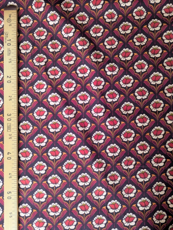 Velours milleraies Hoko à fleurs stylisées écrues et orange, feuillages bordeaux sur fond foncé, motif floral rétro.